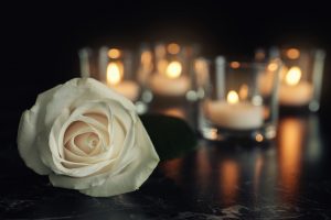 White,Rose,And,Blurred,Burning,Candles,On,Table,In,Darkness,
